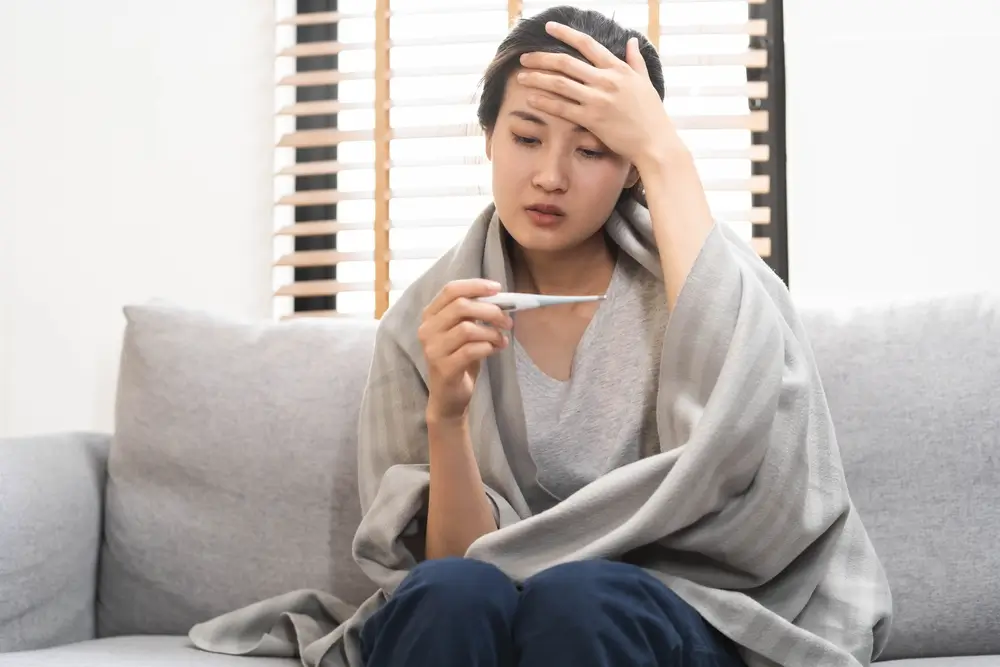 Sick, influenza asian young woman, girl headache have a fever, flu and check thermometer measure body temperature, feel illness sitting on sofa bed at home